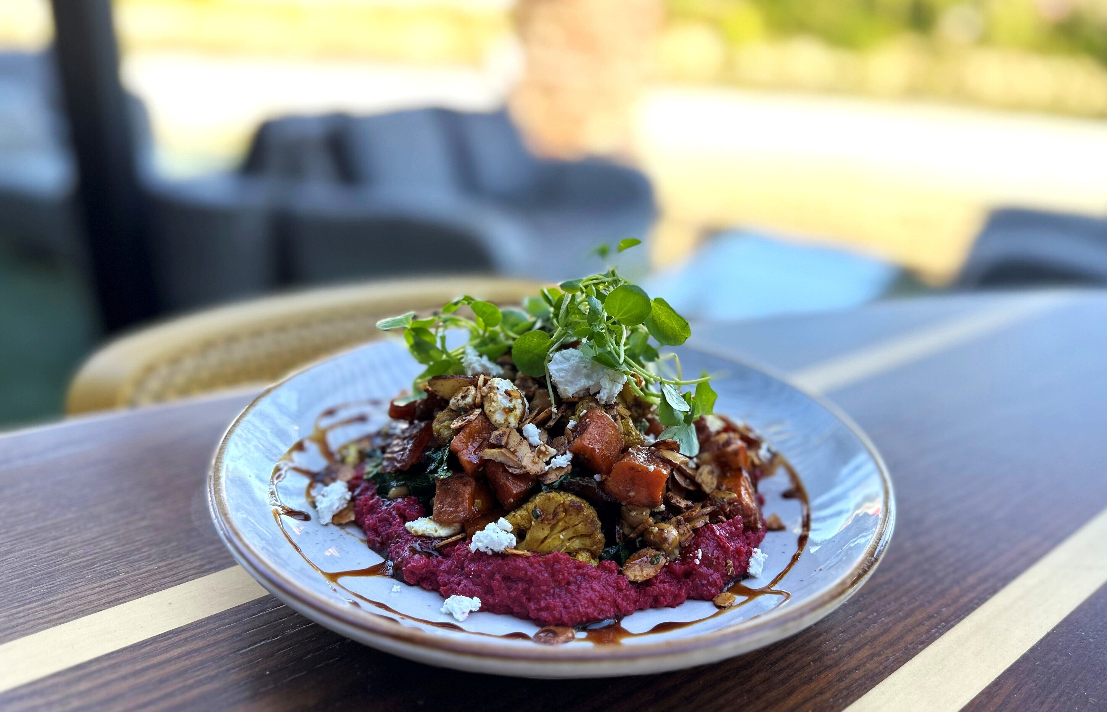 Un plato de comida con diversos ingredientes, entre ellos vegetales verdes, nueces y un puré rojo, sobre una mesa de madera.