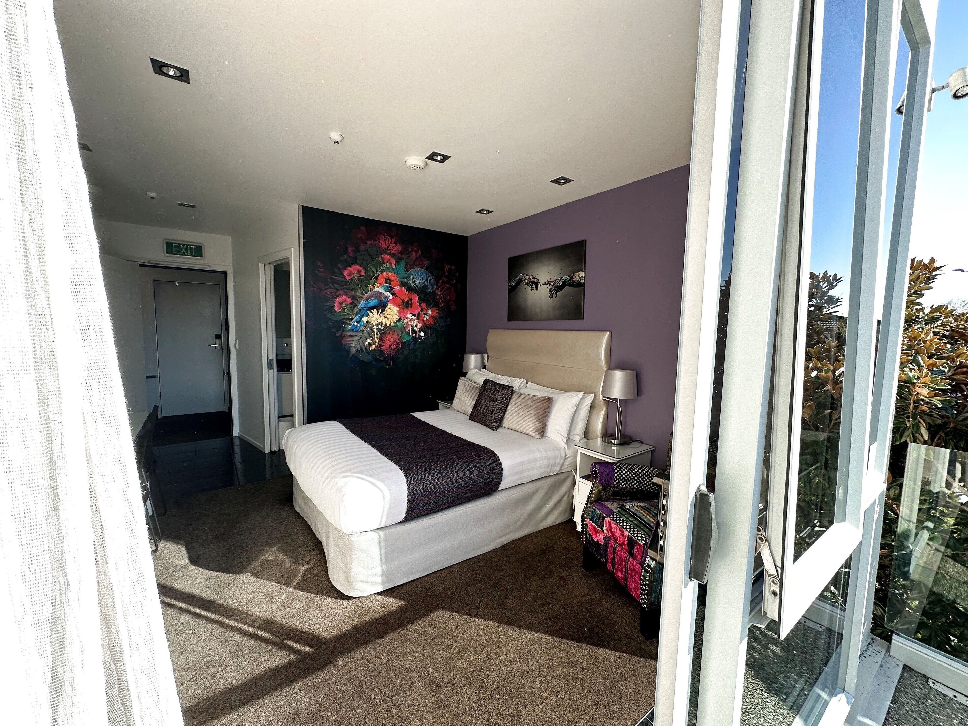 A modern bedroom with a large bed, a nightstand, a wall-mounted lamp, and a painting.