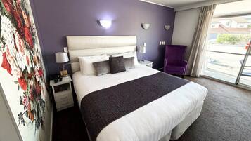 Une chambre d’hôtel avec un grand lit, une table de chevet, une lampe, une chaise et une fenêtre donnant sur un beau paysage.