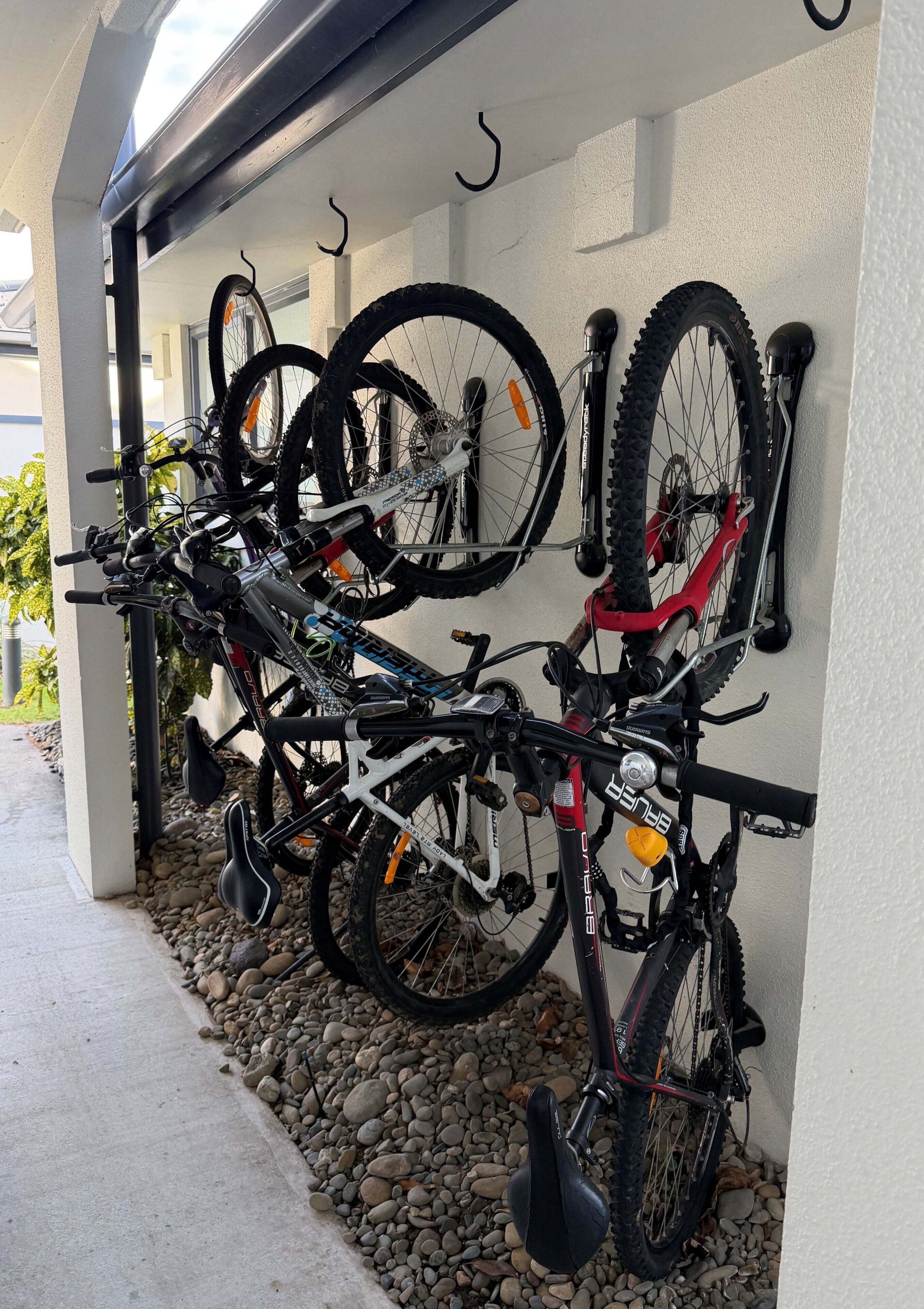 En række cykler hænger på en væg, med en beton gulv og småsten foran.