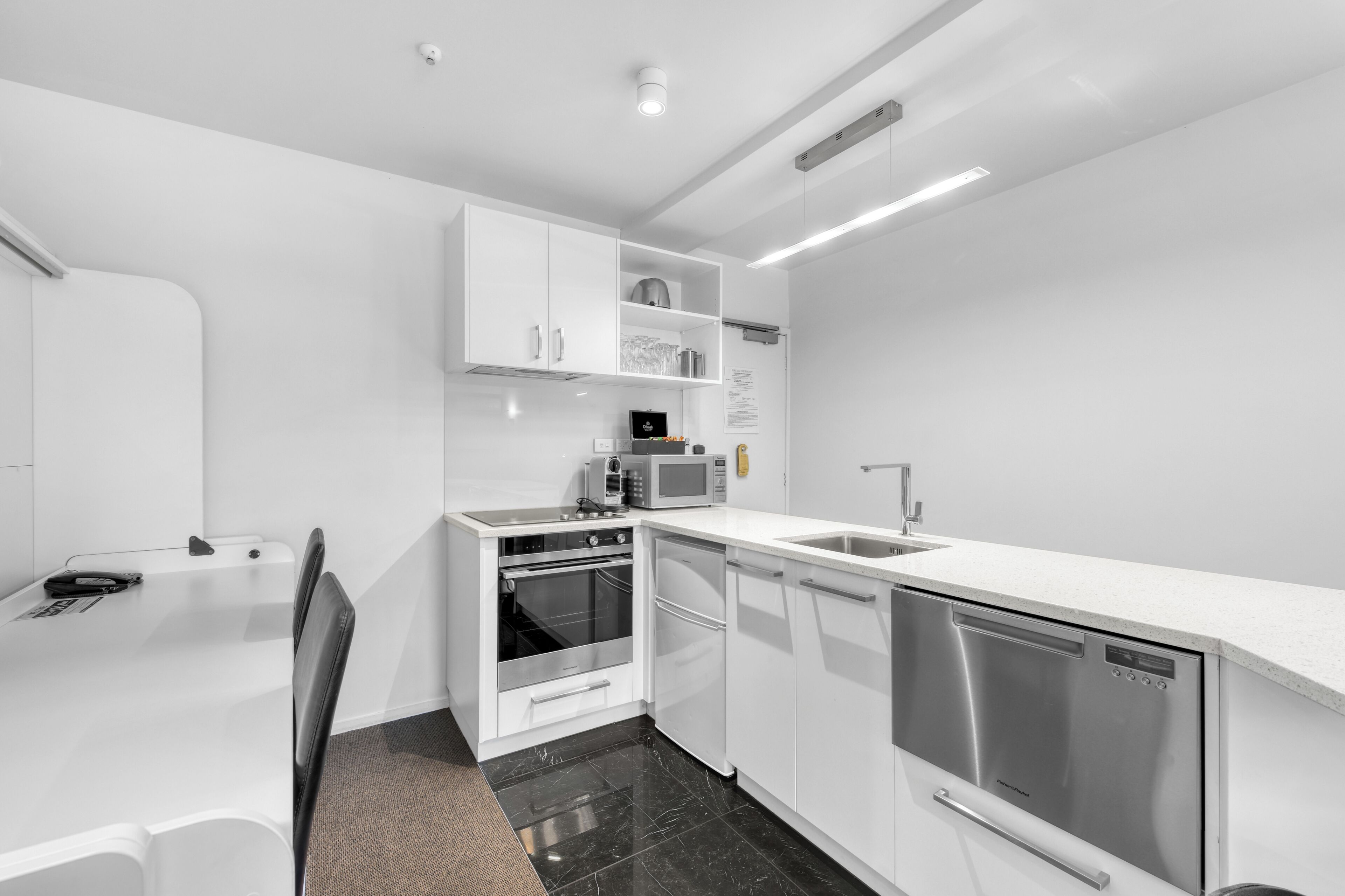 Une cuisine moderne avec des meubles blancs, un four encastré, un four à micro-ondes et un lave-vaisselle.