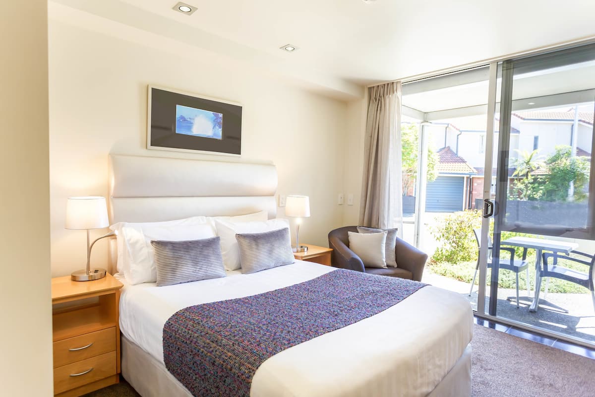 A hotel room with a bed, bedside lamps, a chair, and a view of the outside.