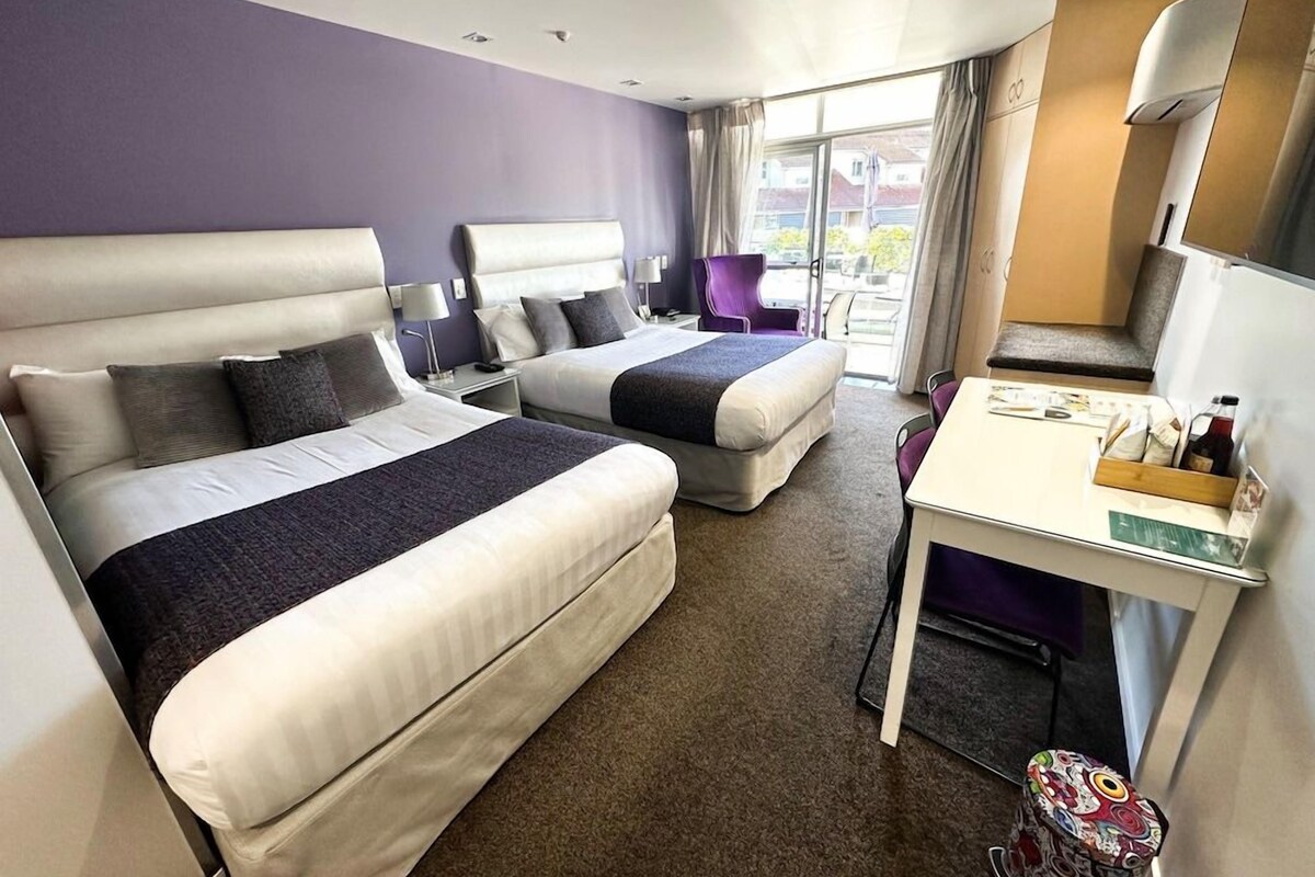 Quarto de hotel com duas camas, uma mesa e uma cadeira.