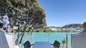 An outdoor seating area with a table and chairs, overlooking a body of water and a hillside with buildings. - Tides Hotel (Nelson)