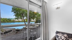 A room with a large window overlooking a pool and greenery. There is a table and chairs outside the window. - Tides Hotel (Nelson)