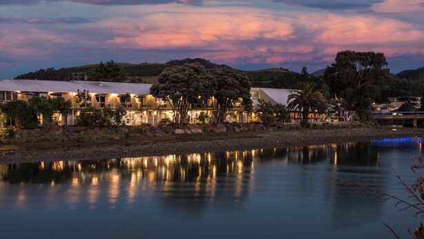 A lakeside hotel with a reflection in the water, surrounded by trees and hills. - Tides Hotel (Nelson)
