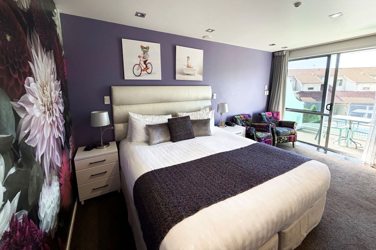 A hotel room with a large bed, a nightstand, a chair, and a balcony with a view.