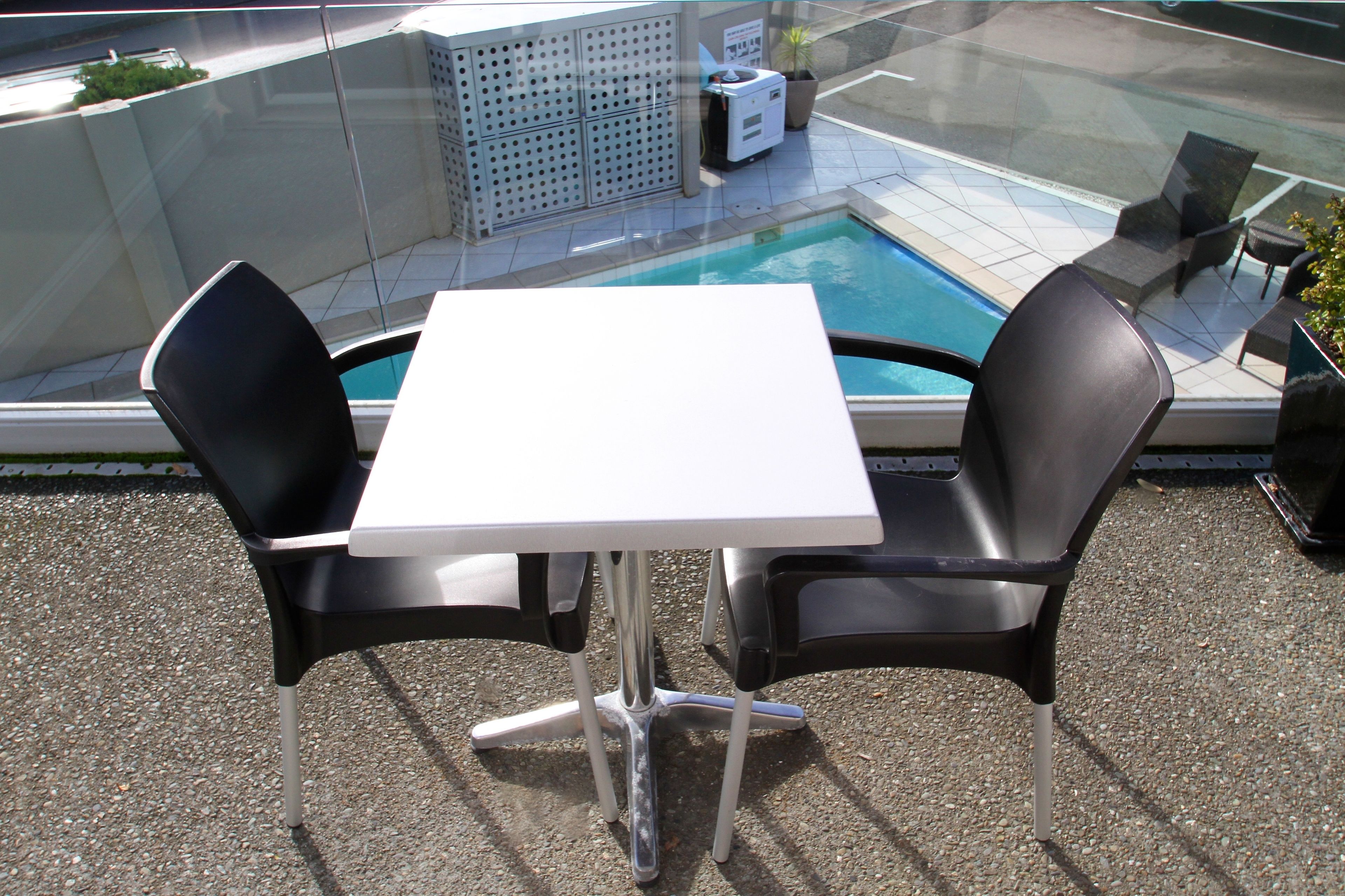 A glass-enclosed outdoor area with a pool, two black chairs, and a white table.