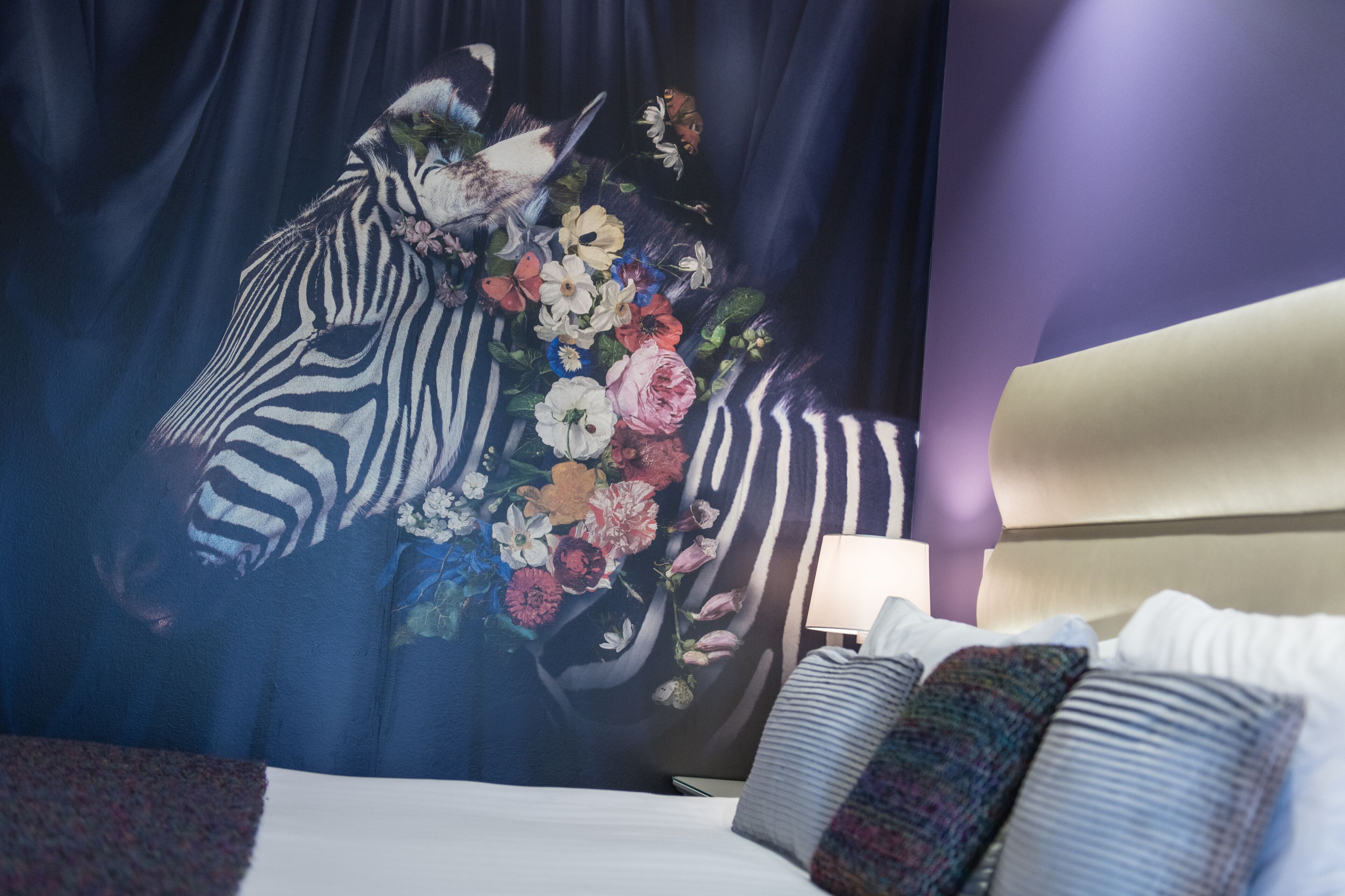 A hotel room with a zebra-striped headboard, a floral tapestry, and a bedside lamp.