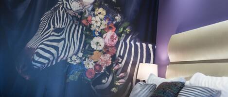 A hotel room with a zebra-striped headboard, a floral tapestry, and a bedside lamp.