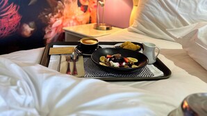 A hotel room with a bed, a tray with breakfast items, a lamp, and a floral wall. - Tides Hotel (Nelson)