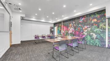 Una sala de conferencias con una larga mesa, sillas moradas y un mural floral colorido en la pared.