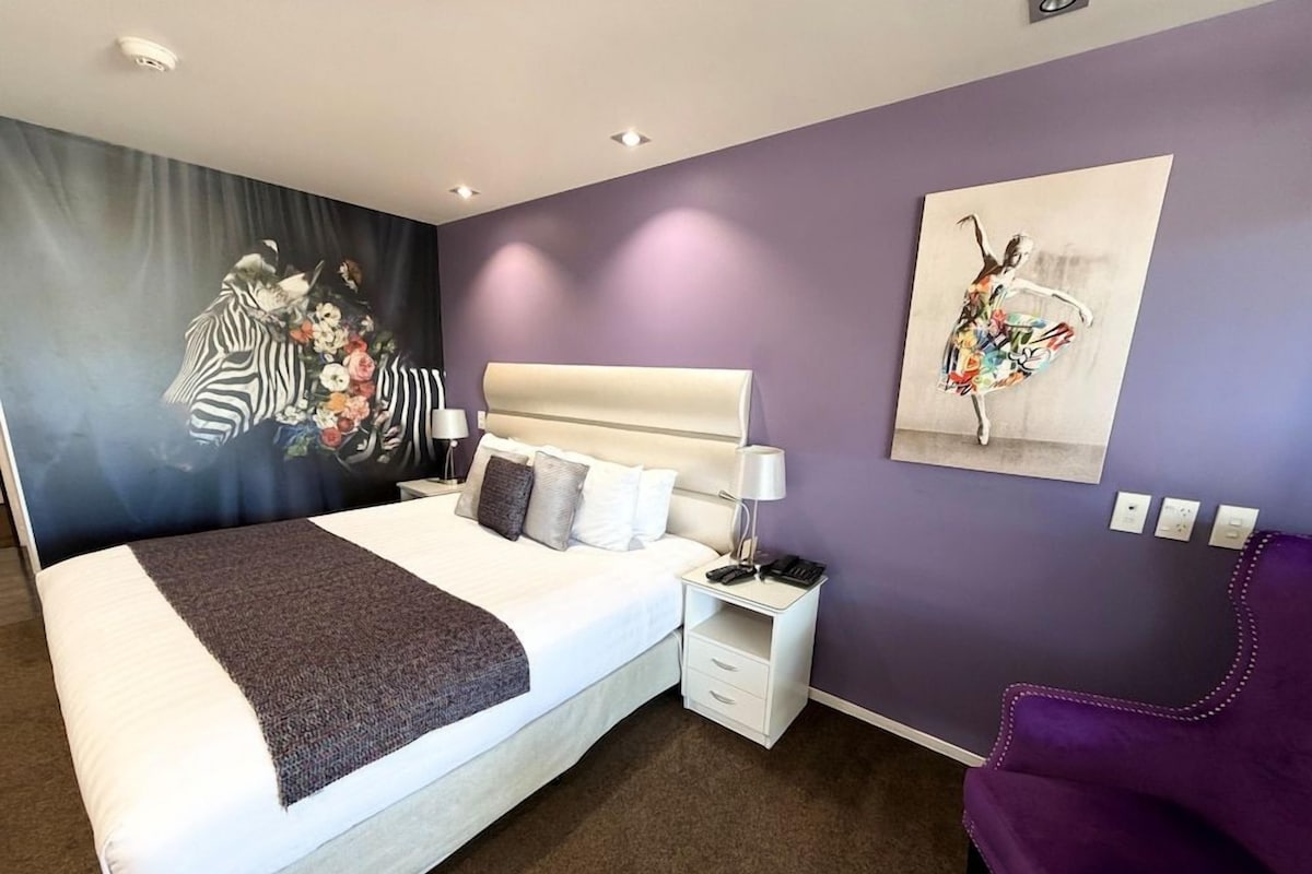 Quarto de hotel com cama, mesa de cabeceira, luminária e obras de arte nas paredes.