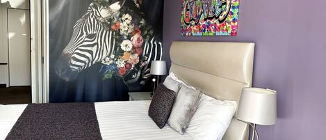 A hotel room with a bed, a headboard, a nightstand with a lamp, a remote control, and a phone.