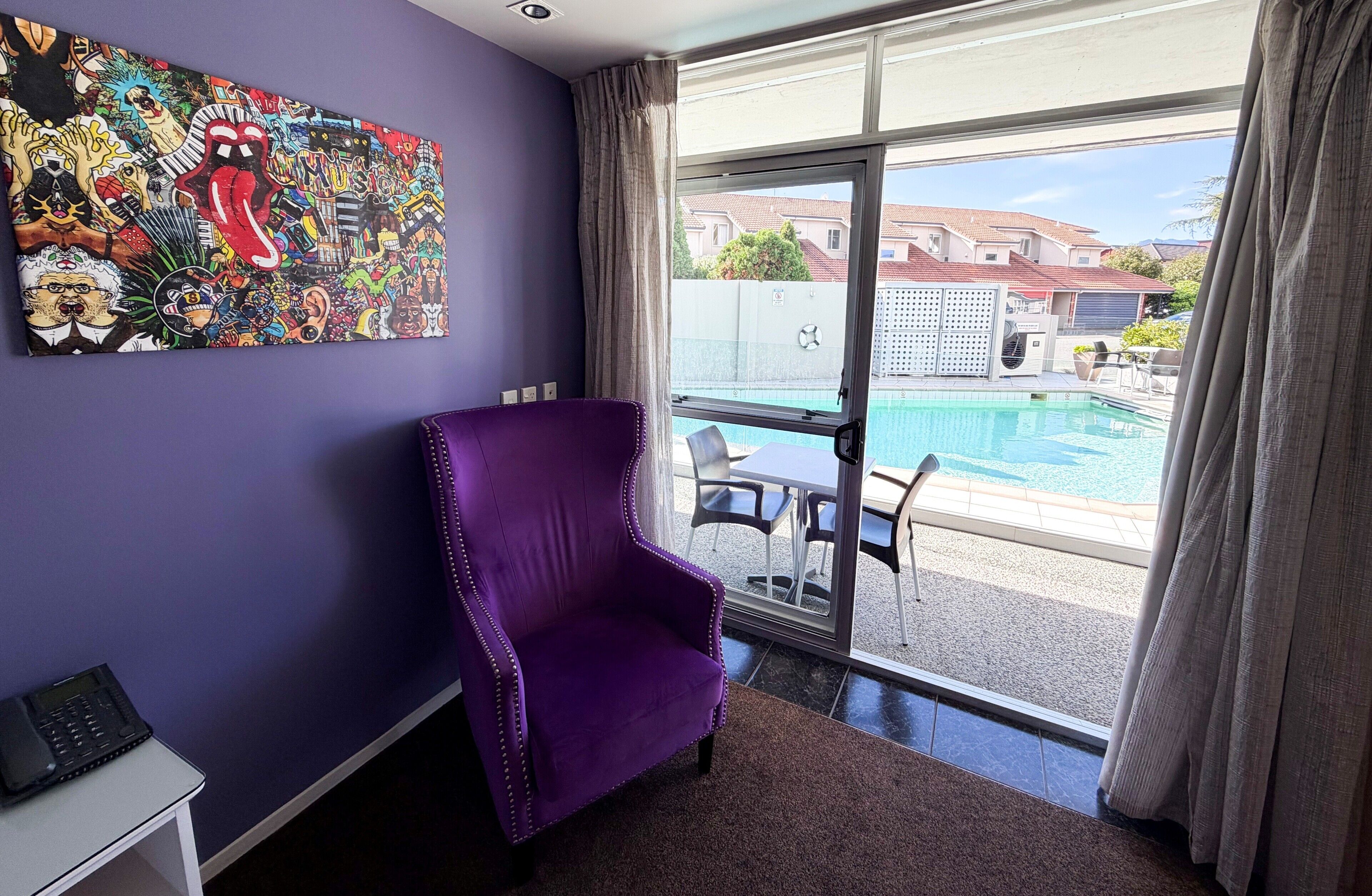 A room with a purple chair, a large abstract painting, a pool view, and a sliding glass door.