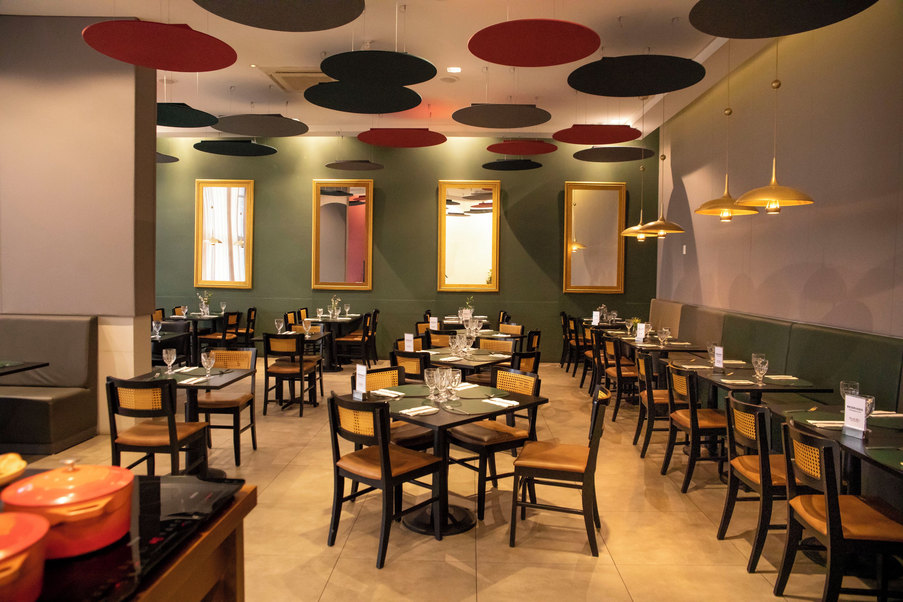 A restaurant interior with multiple dining tables and chairs, ceiling with circular light fixtures, and large mirrors on the walls.