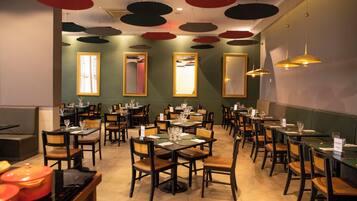A restaurant interior with multiple dining tables and chairs, ceiling with circular light fixtures, and large mirrors on the walls.