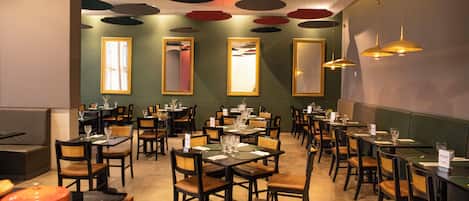 Interior de un restaurante con varias mesas y sillas, techo con lámparas circulares y grandes espejos en las paredes.