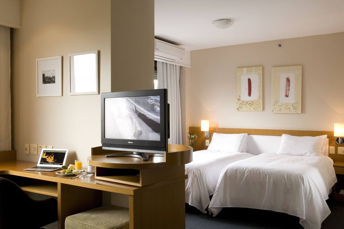Een hotelkamer met een bed, een bureau met een laptop, een televisie en lijstjes met foto's aan de muur.