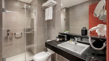 Et moderne badeværelse med en brusekabine i glas, et hvidt toilet, en sort vask med bordplade og en rød accentvæg.