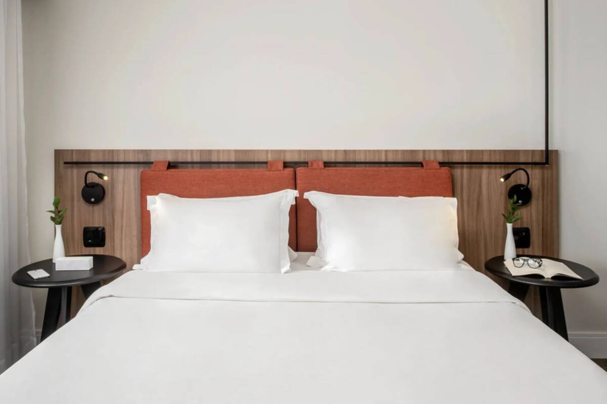 Een hotelkamer met een houten hoofdeinde, witte beddengoed, twee nachtkastjes met lampen, en een kleine plant op elk nachtkastje.