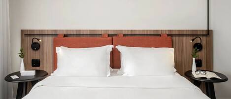 A hotel room with a wooden headboard, white bedding, two bedside tables with lamps, and a small plant on each table.