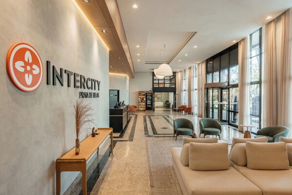 Een moderne lobby met een receptiebalie, een zithoek en grote ramen.
