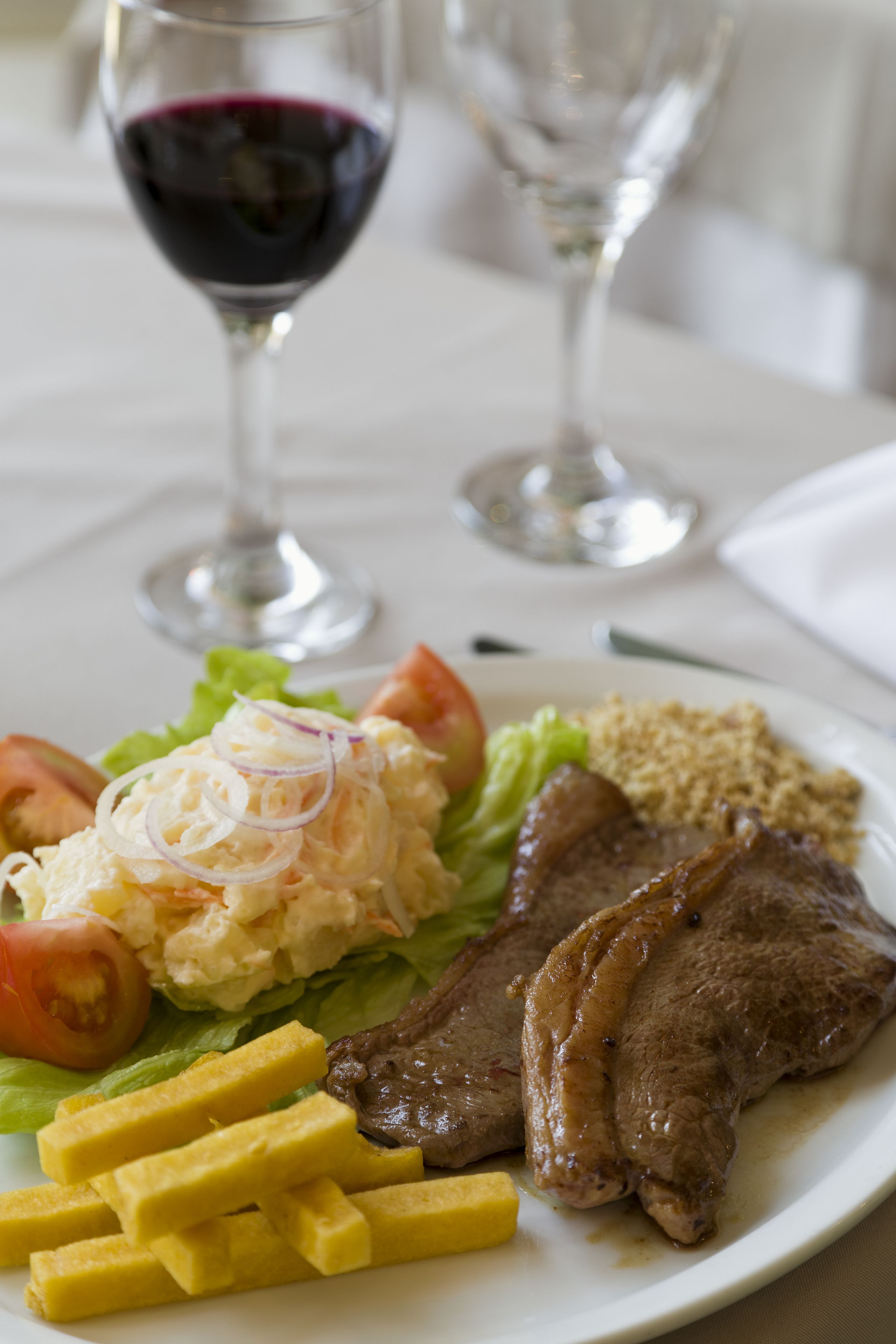 Une assiette de nourriture comprenant un steak, des frites et une salade, accompagnée d’un verre de vin rouge.