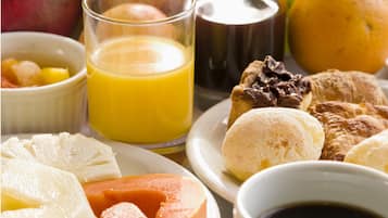 Uma mesa de café da manhã com frutas variadas, um copo de suco de laranja, uma xícara de café e doces.