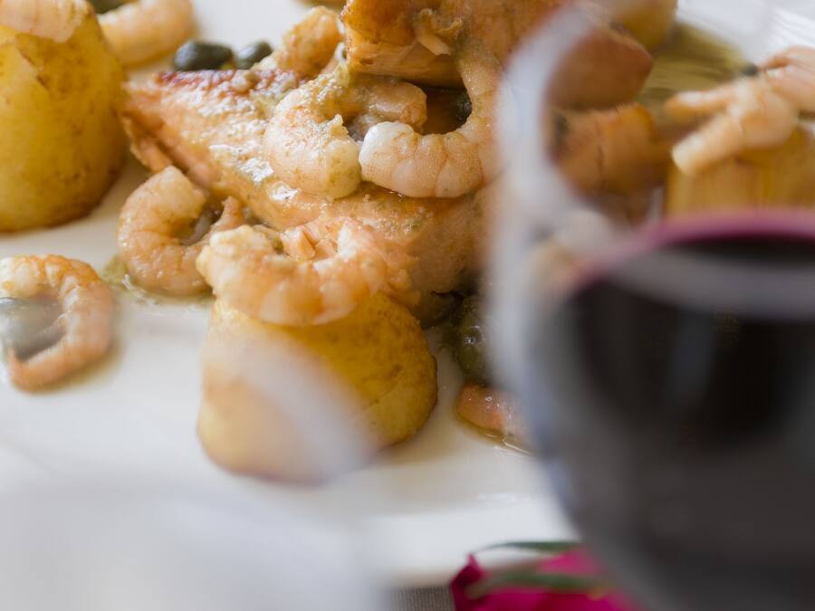 Un plato de comida con camarones y papas, una copa de vino tinto y una rosa sobre la mesa.