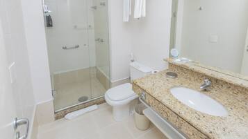 Uma casa de banho moderna com chuveiro de vidro, sanita e bancada de granito com lavatório.