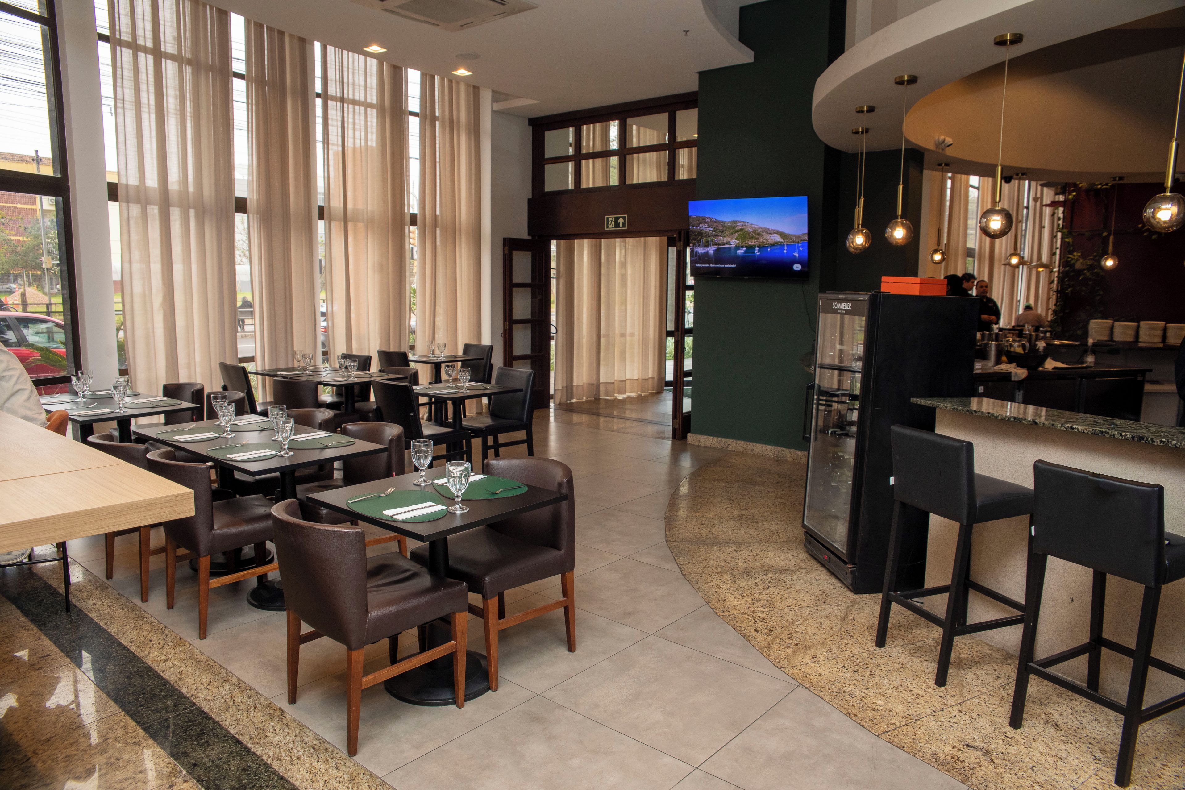 A restaurant with tables set for dining, a bar area, and a television screen displaying a scenic view.