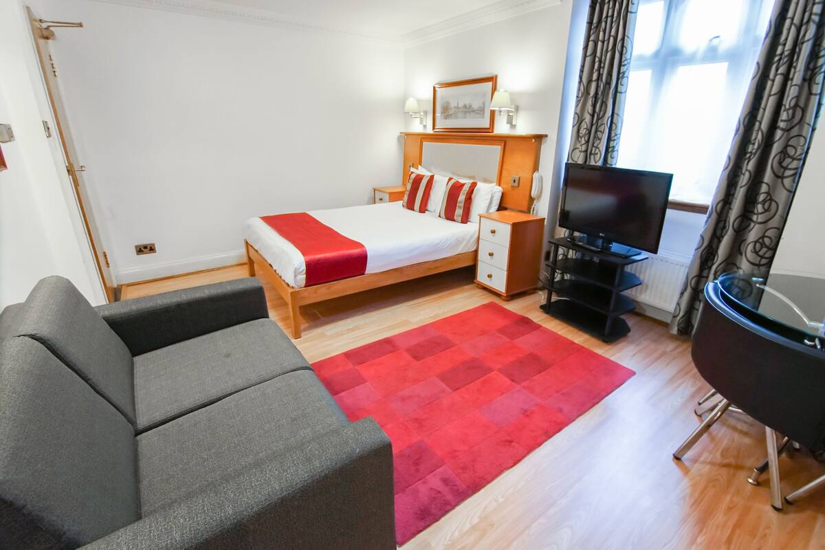 Hotellihuone, jossa on sänky, televisio, sohva ja punainen matto.