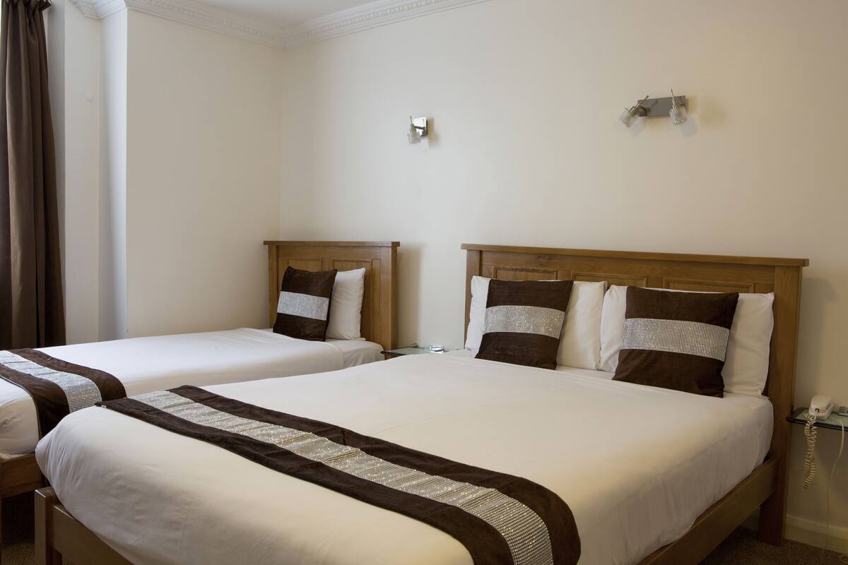 Hotellihuoneessa on kaksi erillistä sänkyä, joissa on molemmissa puinen pääty sekä valkoiset vuodevaatteet ja ruskea koristelista. Oikealla puolella on yöpöytä, jossa on lamppu ja puhelin.