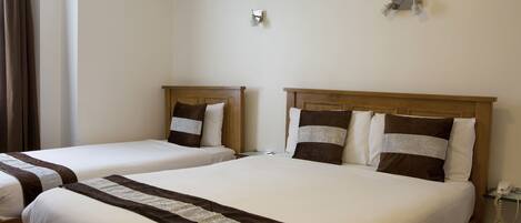 A hotel room with two single beds, each with a wooden headboard, white bedding, and a brown decorative strip. There is a bedside table with a lamp and a phone on the right side.