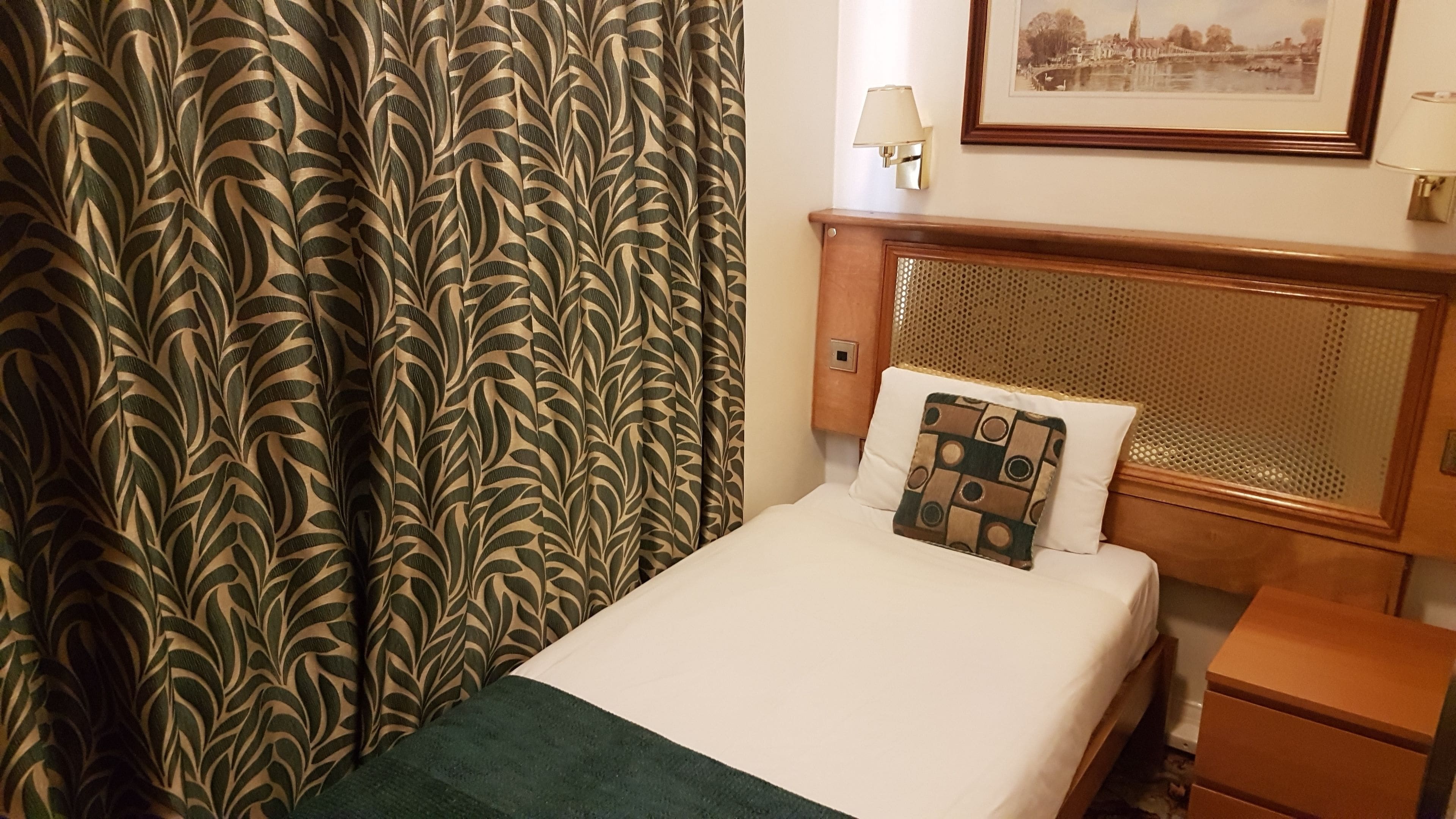 A hotel room with a bed, a nightstand, a lamp, and a framed picture on the wall.