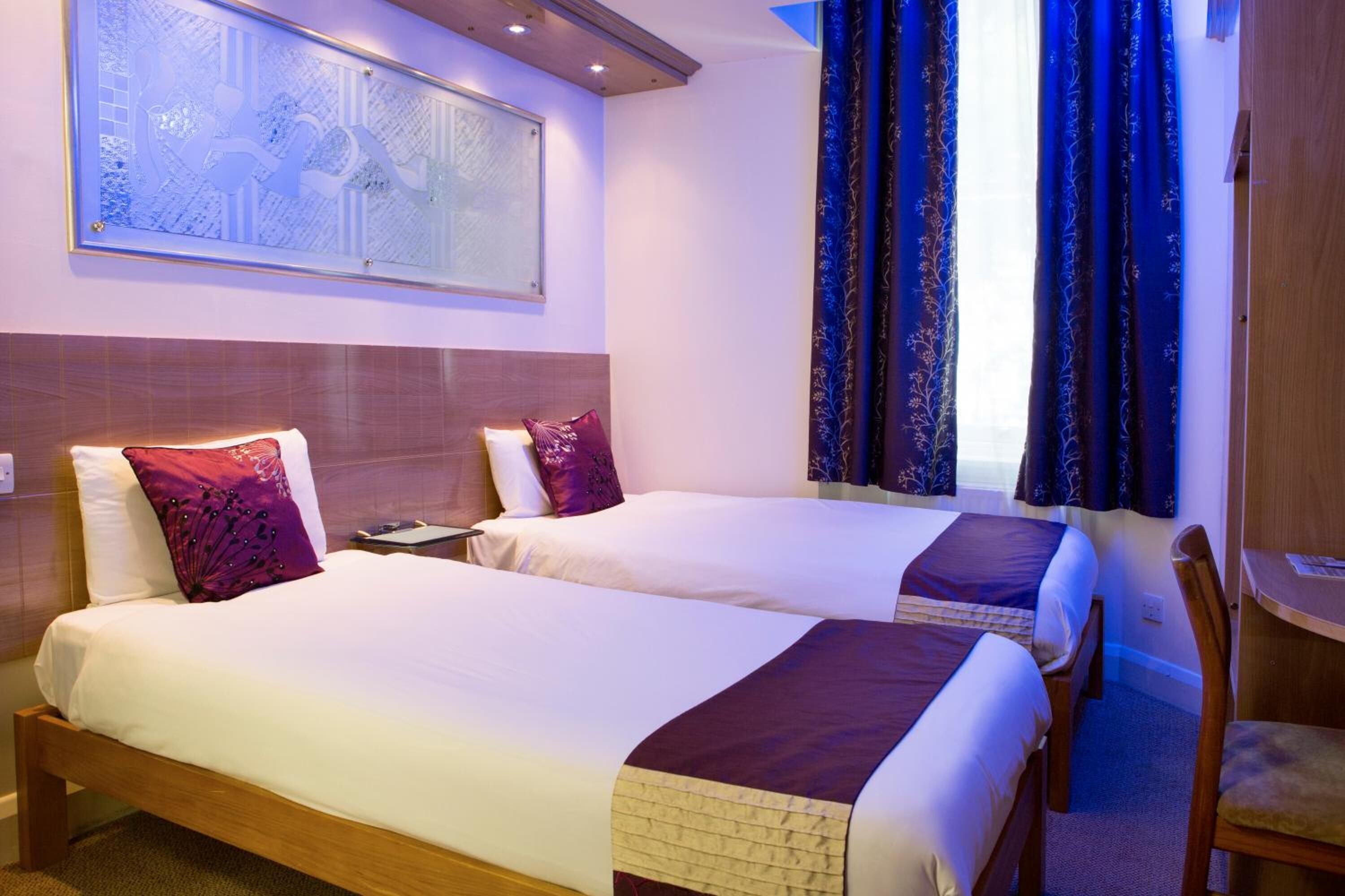 A hotel room with two beds, a wooden headboard, a nightstand, a desk, and a chair.