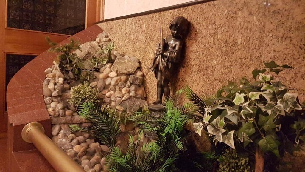 A statue of a child holding a staff, surrounded by rocks and plants.