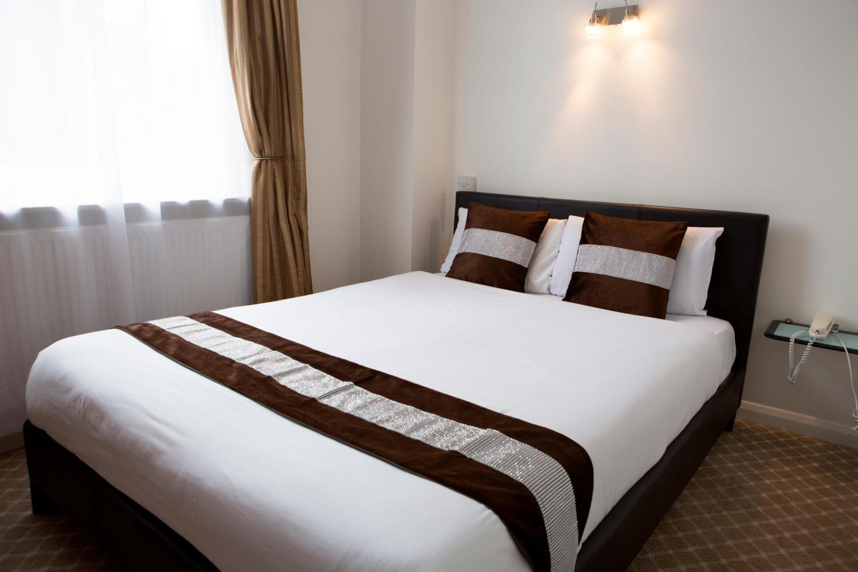 A hotel room with a large bed, a bedside table with a lamp, and a window with curtains.