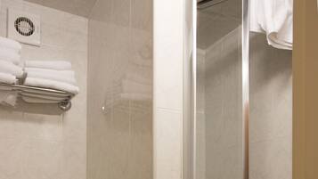 A bathroom with a toilet, a glass shelf with towels, and a glass-enclosed shower area.