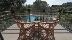 A wicker chair with a table on a balcony overlooking a swimming pool.
