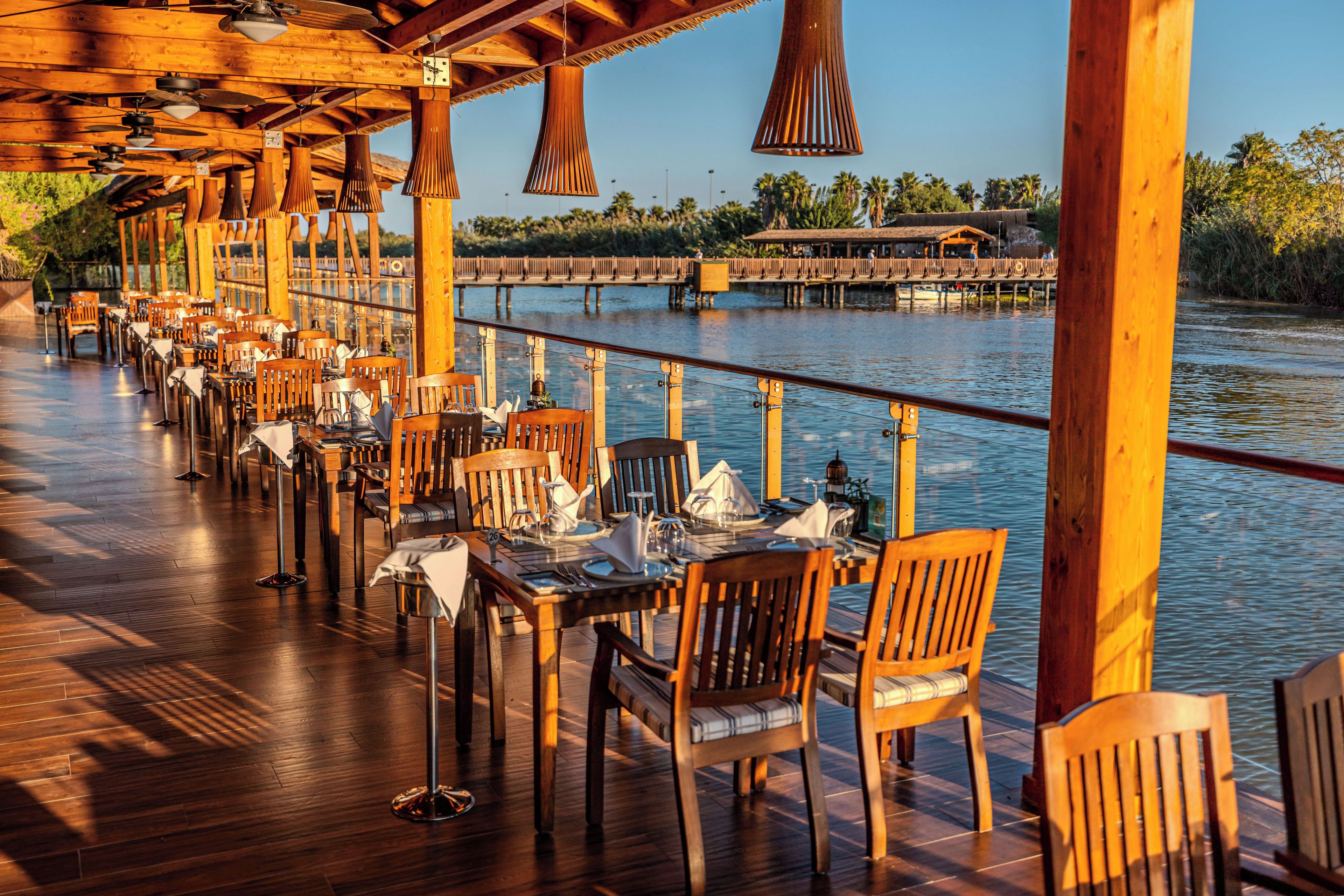 Un restaurant en plein air avec des tables et des chaises en bois, donnant sur un plan d’eau.
