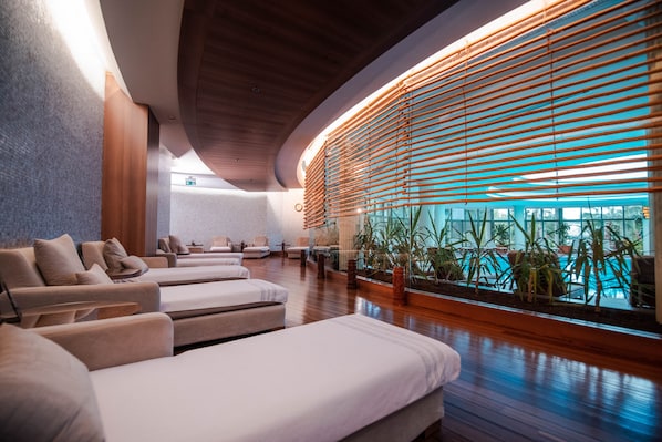 A spa area with multiple massage beds, wooden paneling, and a view of the pool.