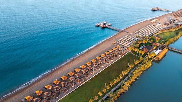 An aerial view of a beachside resort with rows of thatched-roof huts, a pier, and a dock. - Gloria Golf Resort - All Inclusive (Serik)