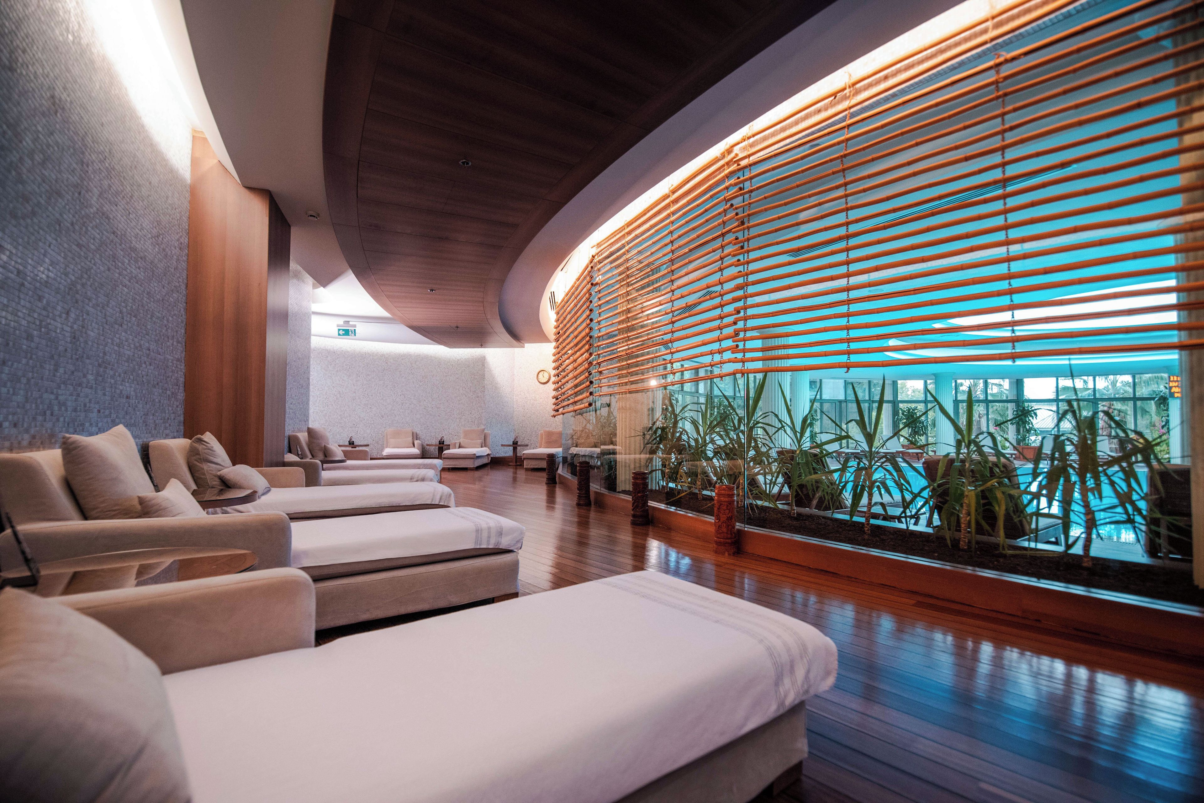 A spa area with massage chairs, a wooden ceiling, and a view of a pool through large windows.
