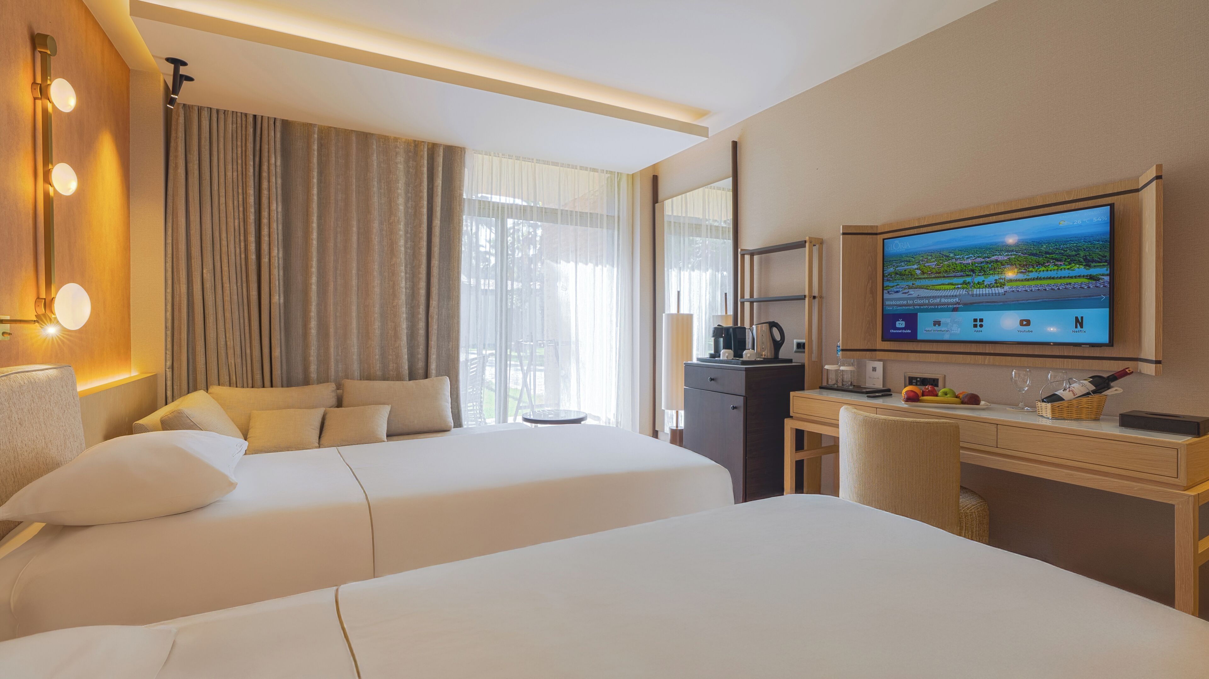 A hotel room with two beds, a desk, a TV, and a view of the outdoors.