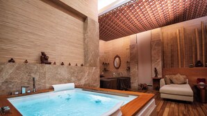 A spa room with a large bathtub, wooden flooring, and a seating area with a sofa and table.