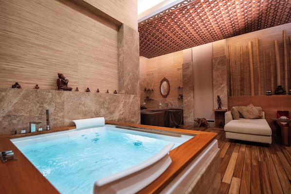 A spa room with a large bathtub, wooden flooring, and a seating area with a sofa and table.