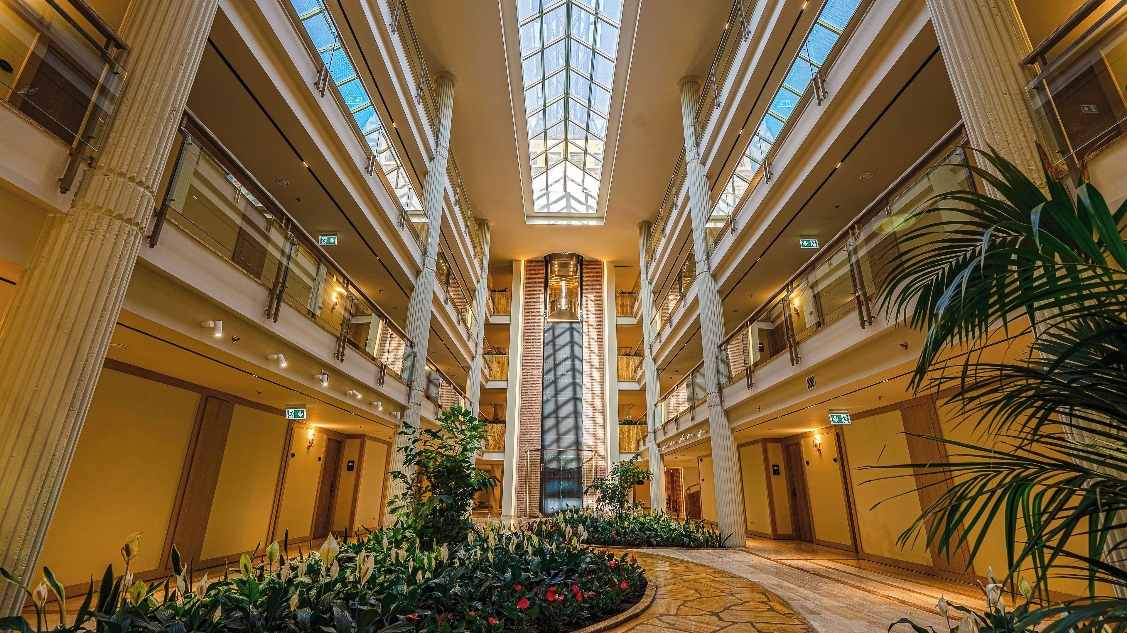 A hotel atrium with a central elevator, multiple floors, and a central garden area.