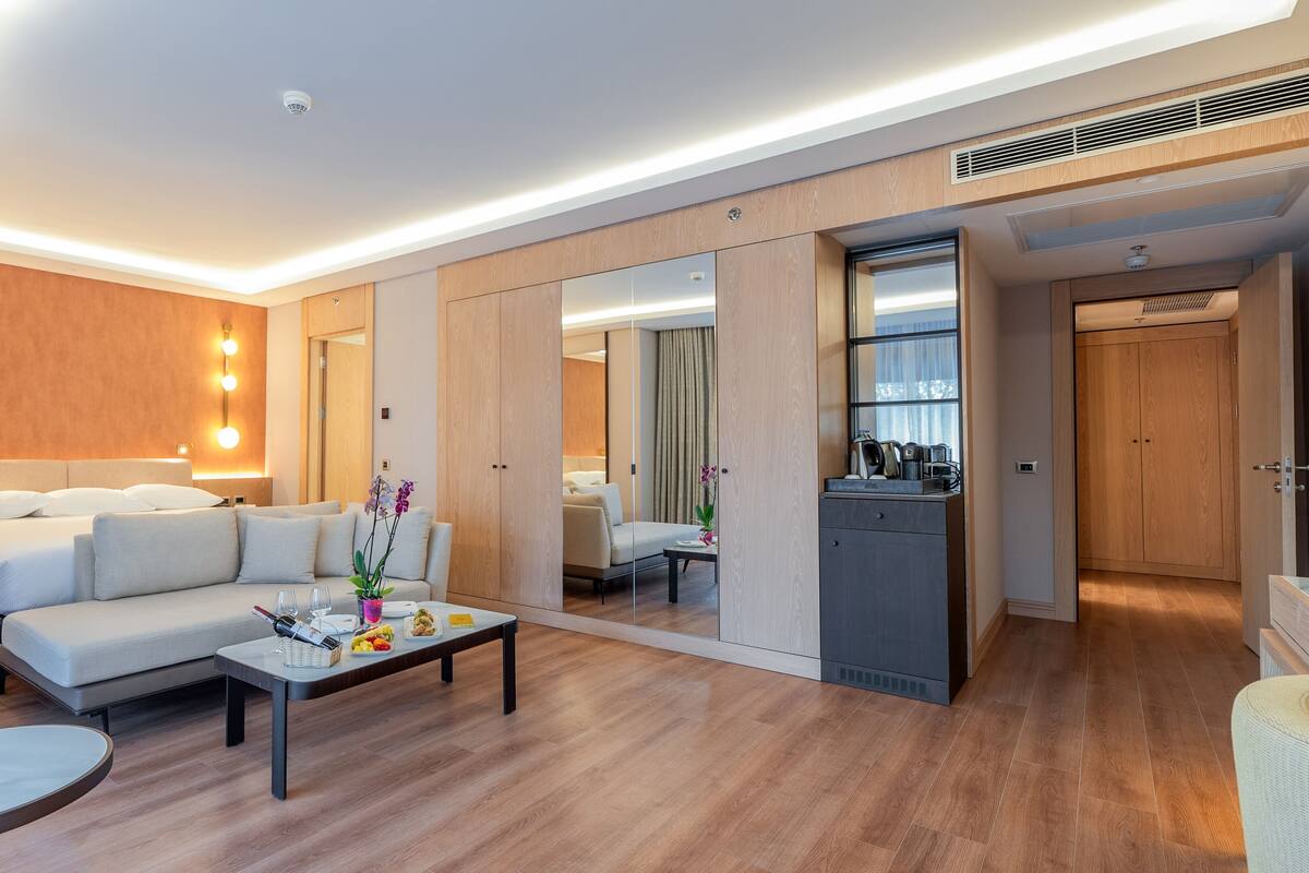 A modern hotel room with a bed, sofa, coffee table, and a mirror.